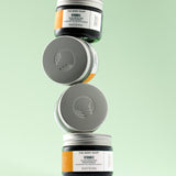 Three jars of The Body Shop Vitamin C Glow Boosting Moisturiser 50 ML stacked on a textured surface against a soft green back