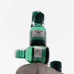 Stack of The Body Shop Tea Tree Oil 20 ML on concrete block, showcasing vibrant green branding against clean background