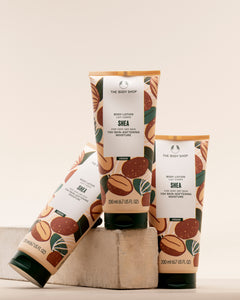 Three tubes of The Body Shop Shea Body Lotion 200 ML artistically arranged on a stone surface against a soft, muted backgroun