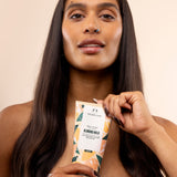 Woman holds The Body Shop Almond Milk Body Lotion 200ml against soft peach-toned background