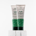Two tubes of The Body Shop Tea Tree 3-in-1 Wash-Scrub-Mask 125ml displayed on a textured pedestal against a clean background.