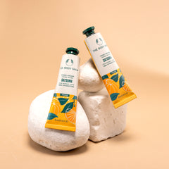 Two tubes of The Body Shop Satsuma Hand Cream 30 ML displayed against a soft warm-toned background with stones