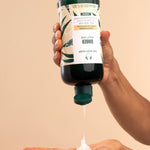 Hand pouring The Body Shop Ginger Scalp Care Conditioner 440 ML into palm against a neutral background.