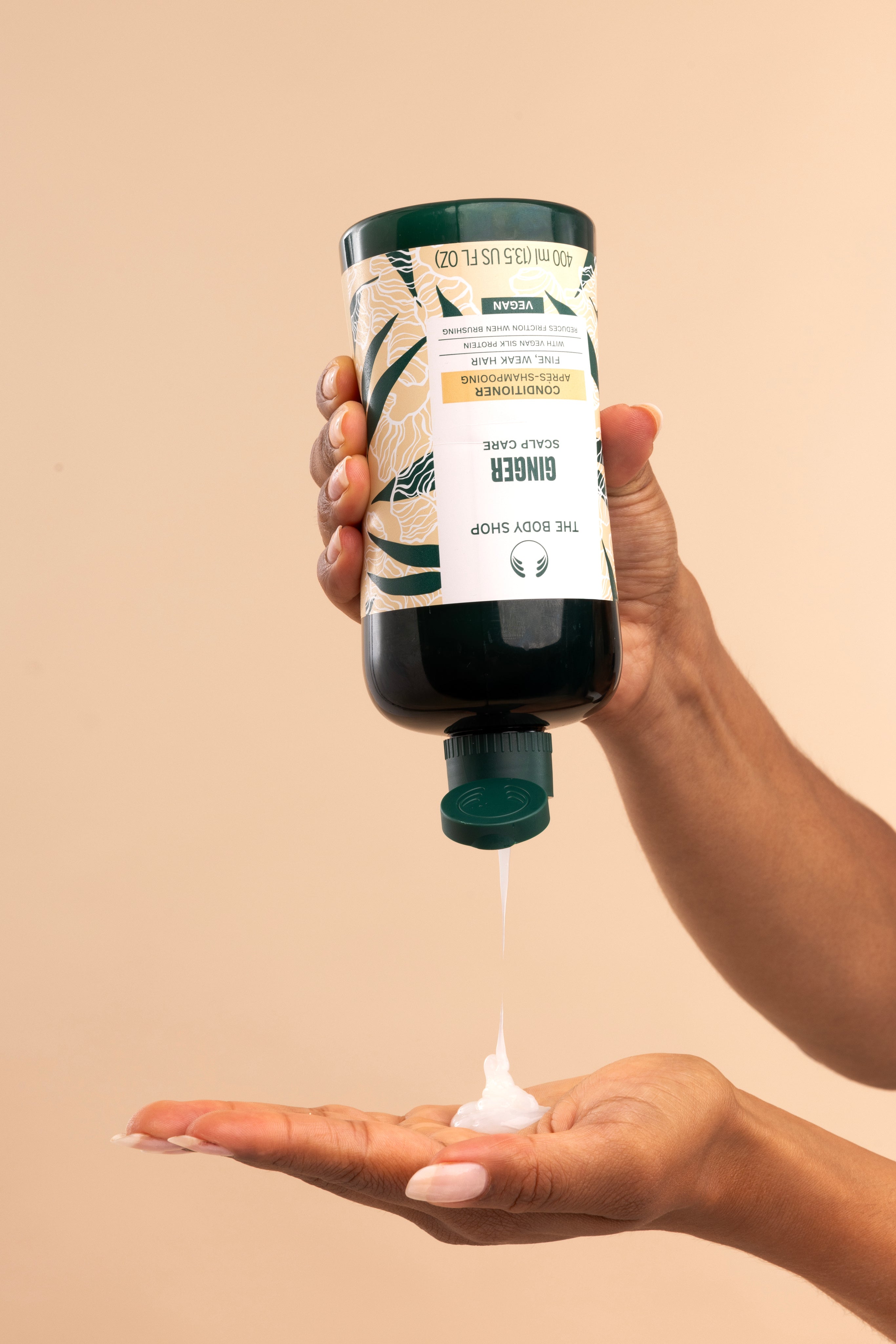 Hand pouring The Body Shop Ginger Scalp Care Conditioner 440 ML into palm against a neutral background.