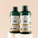 Two bottles of The Body Shop Ginger Scalp Care Conditioner 250 ML displayed on white pedestal against soft beige background.