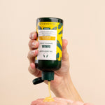 Hand dispensing The Body Shop Banana Truly Nourishing Shampoo 250 ML into palm.