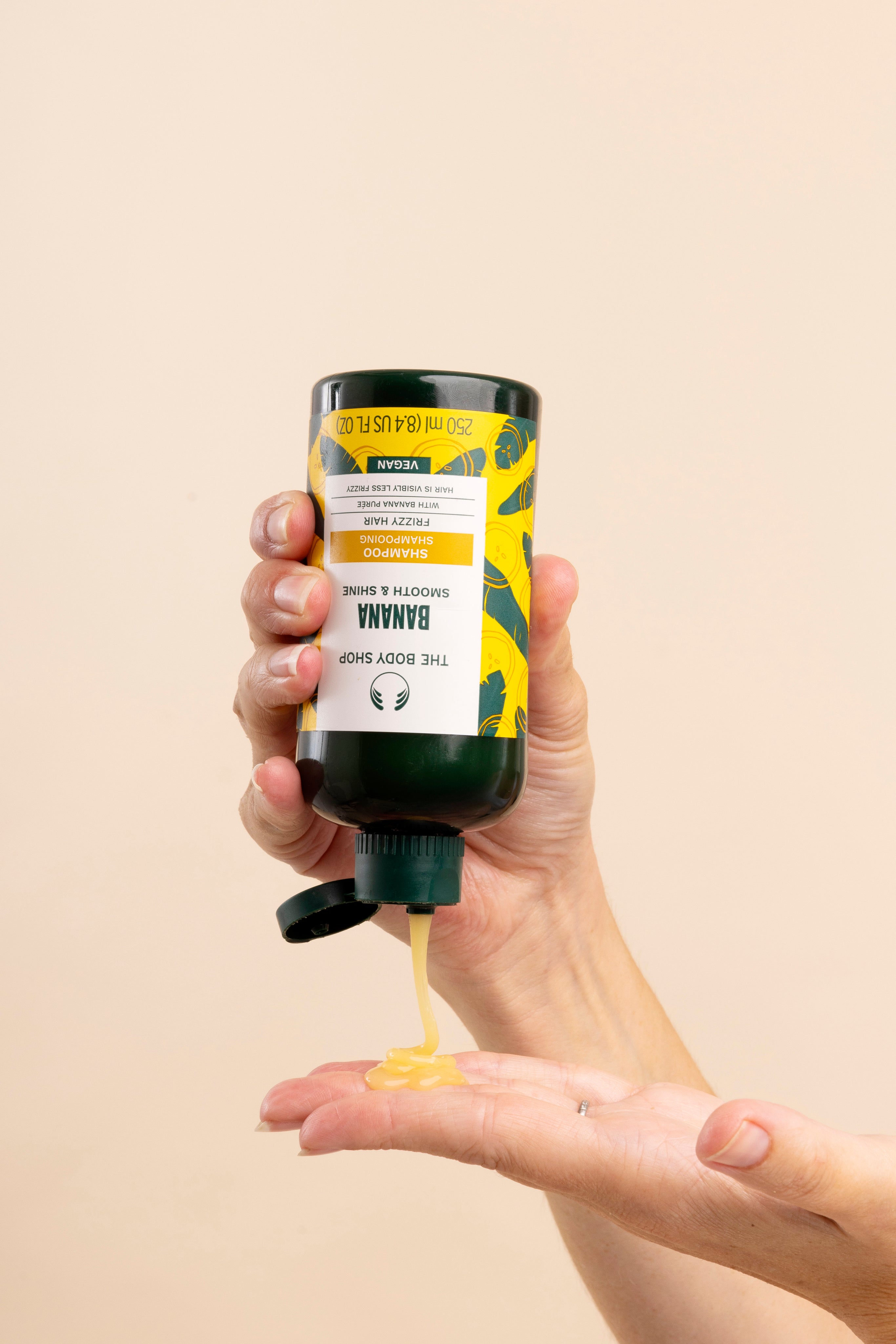 Hand dispensing The Body Shop Banana Truly Nourishing Shampoo 250 ML into palm.