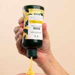 Hand dispensing The Body Shop Banana Truly Nourishing Conditioner 250 ML against a soft neutral background
