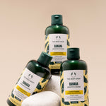 Three bottles of The Body Shop Banana Smooth & Shine Conditioner 250 ML displayed on a pedestal of stones against soft beige