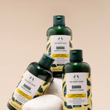 Three bottles of The Body Shop Banana Smooth & Shine Conditioner 250 ML displayed on a pedestal of stones against soft beige