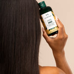 Woman holding The Body Shop Ginger Shampoo 250 ML against soft neutral background