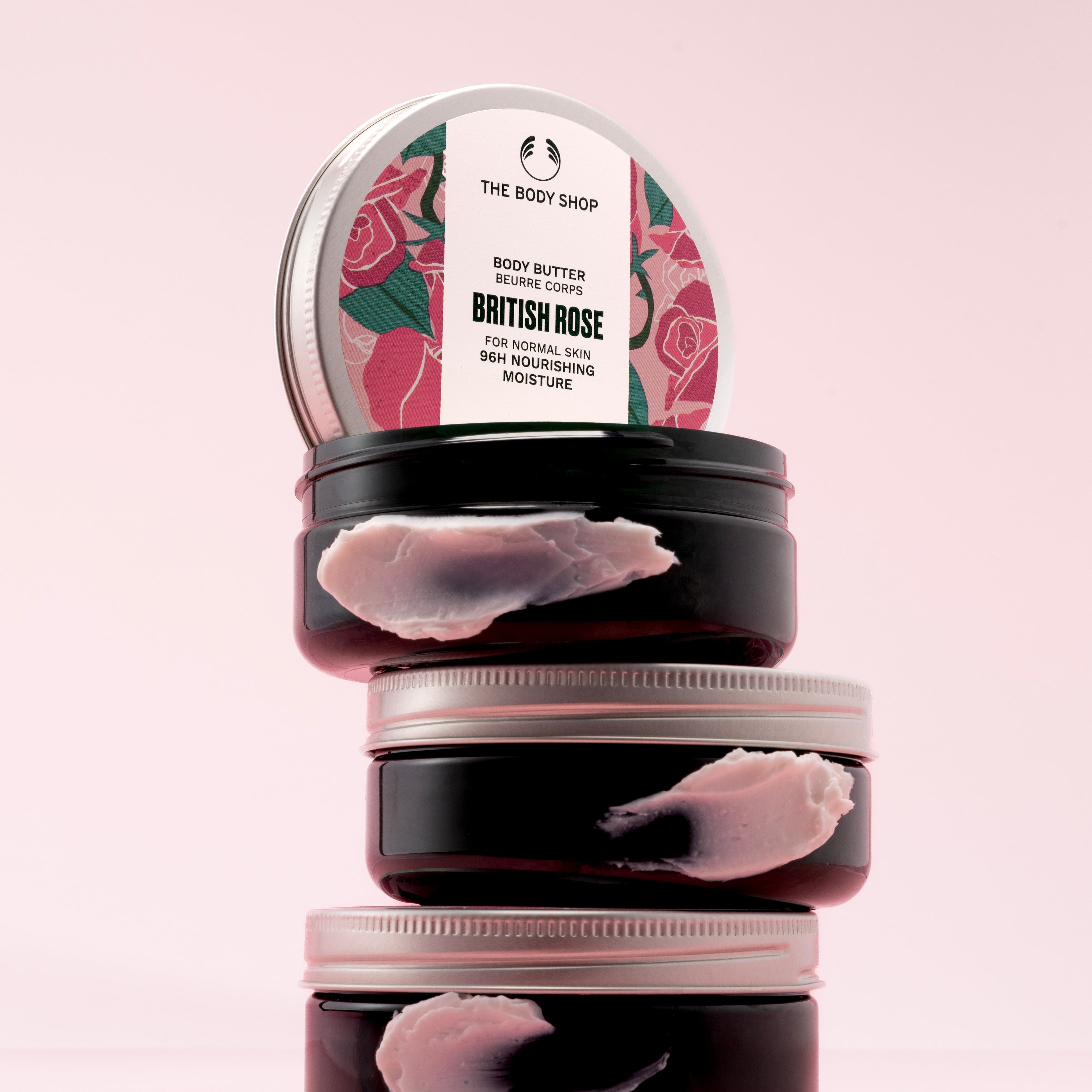 A stack of The Body Shop British Rose Body Butter 200ml against a soft pink backdrop.