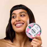 Woman smiling while holding The Body Shop British Rose Body Butter 200 ML against a soft, neutral background.