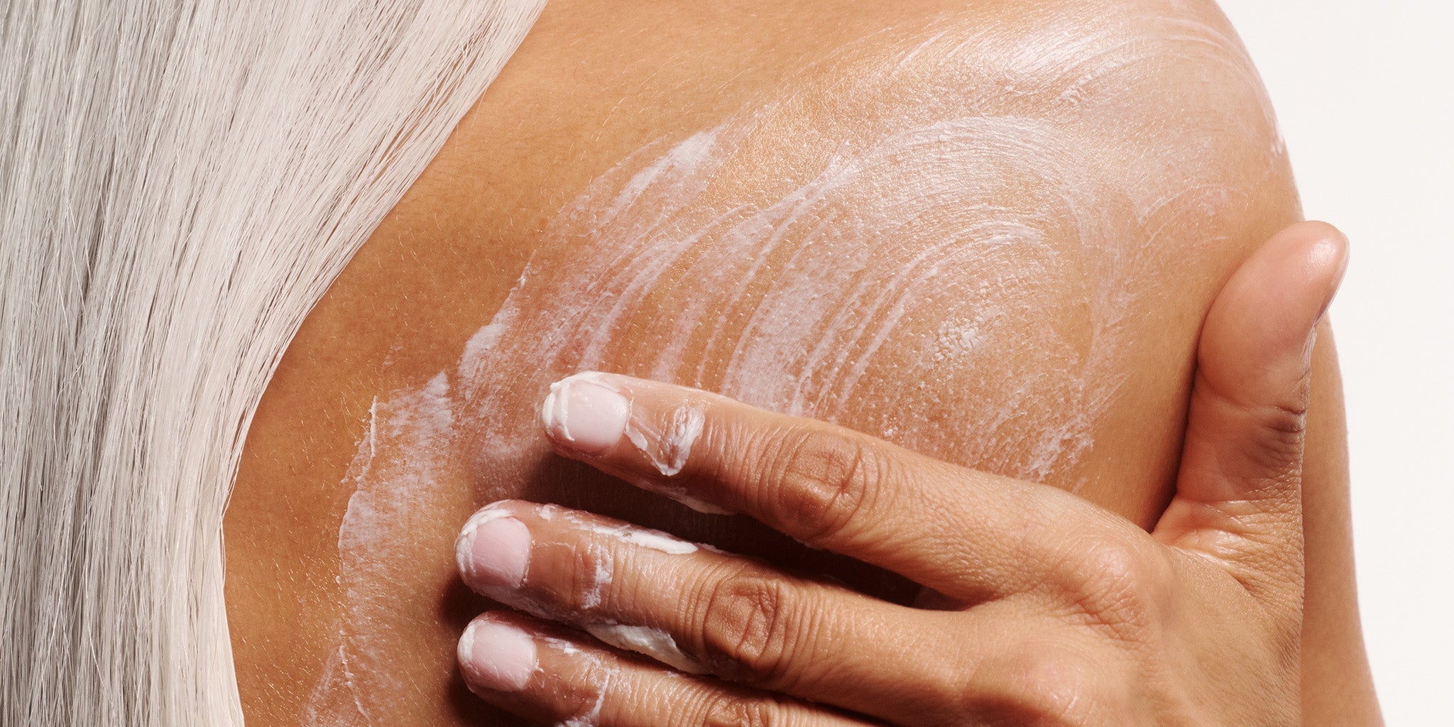 Woman applying Shea Body Butter to her shoulder and back with a beige background