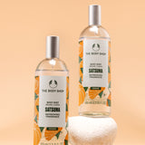 Visually appealing display of The Body Shop Satsuma Body Mist 100 ML against soft orange background