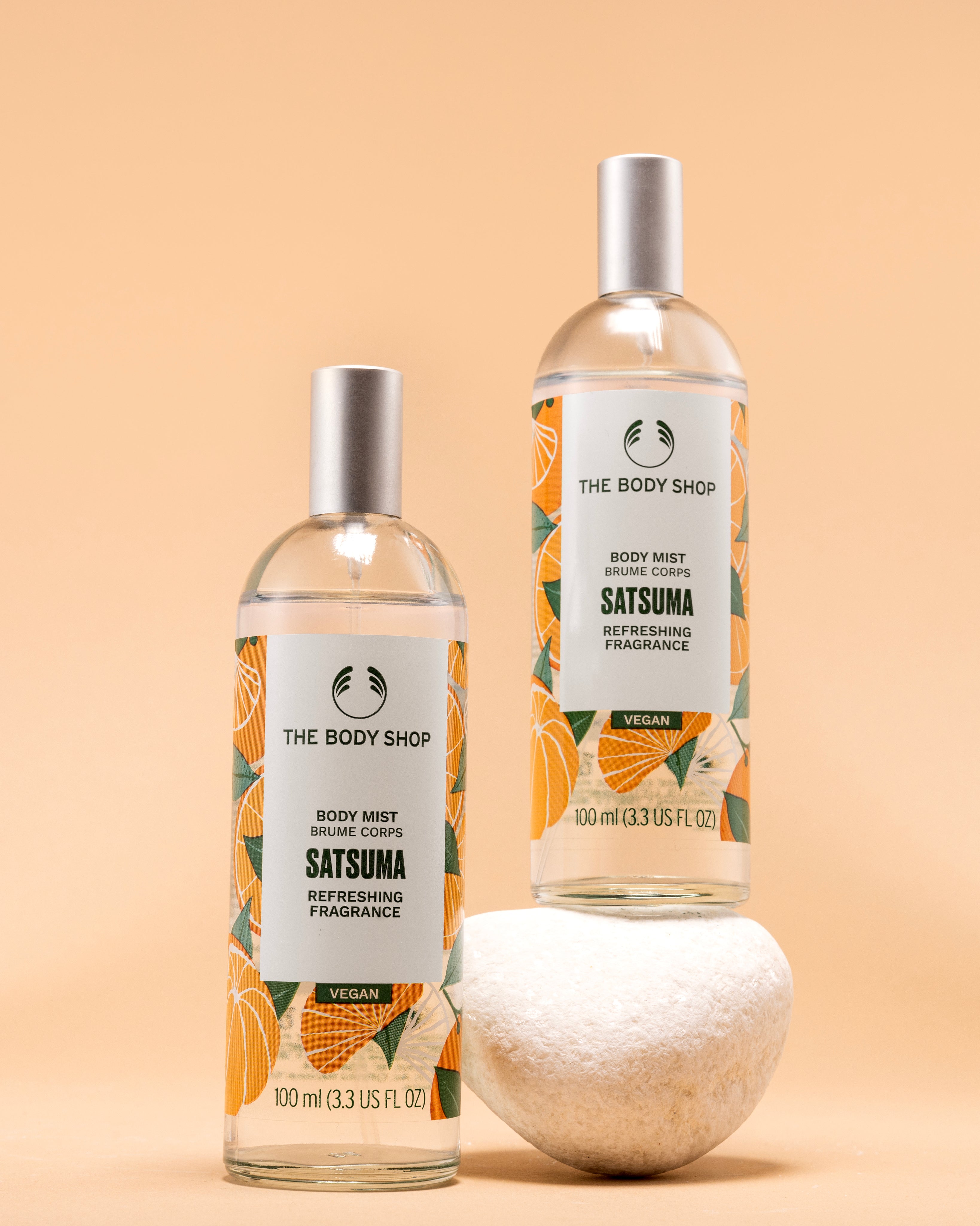 Visually appealing display of The Body Shop Satsuma Body Mist 100 ML against soft orange background