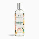 A bottle of The Body Shop Pink Grapefruit Body Mist 100 ML against a vibrant, fruity background.