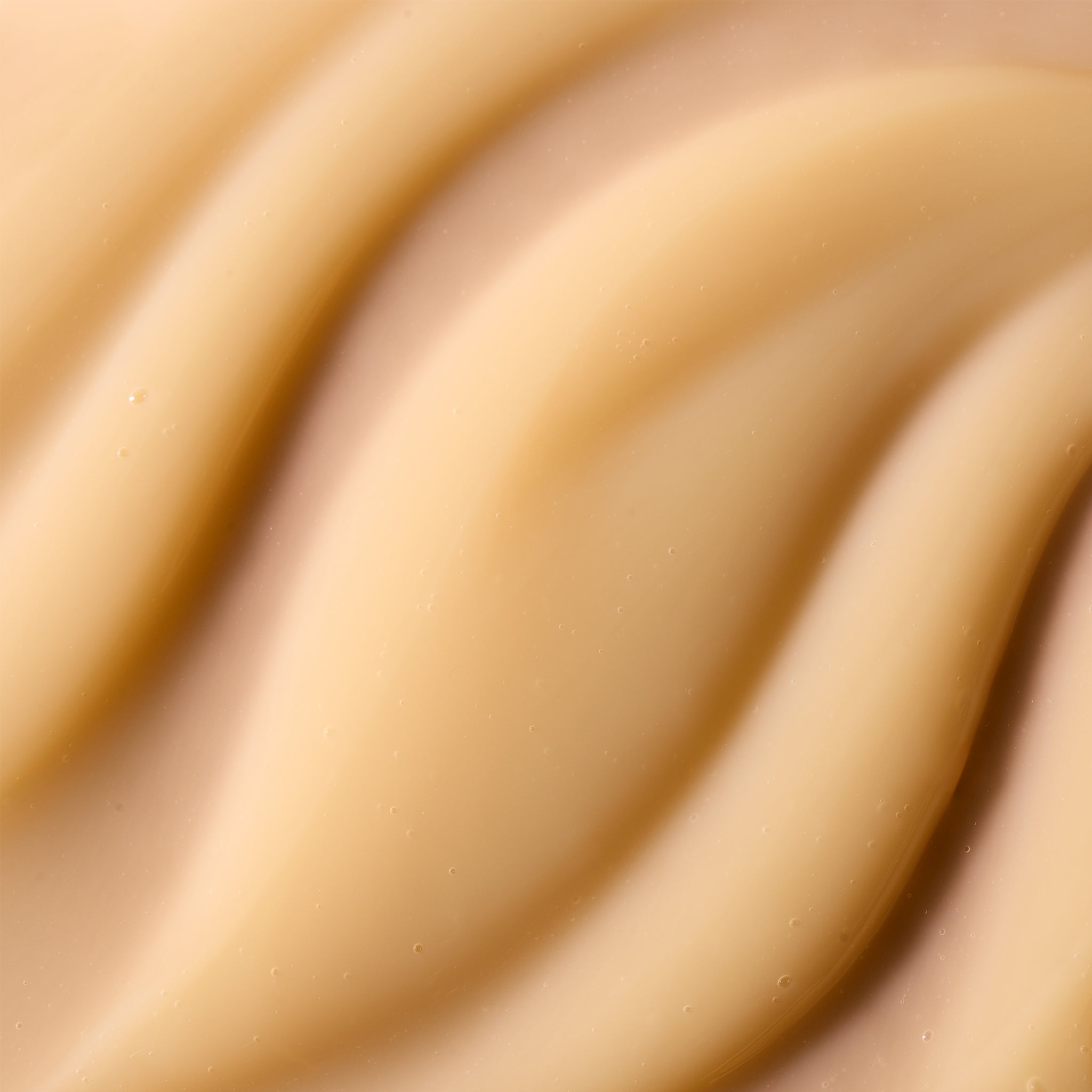 A close-up texture shot of a smooth, creamy beige cosmetic cream with soft, flowing ridges.