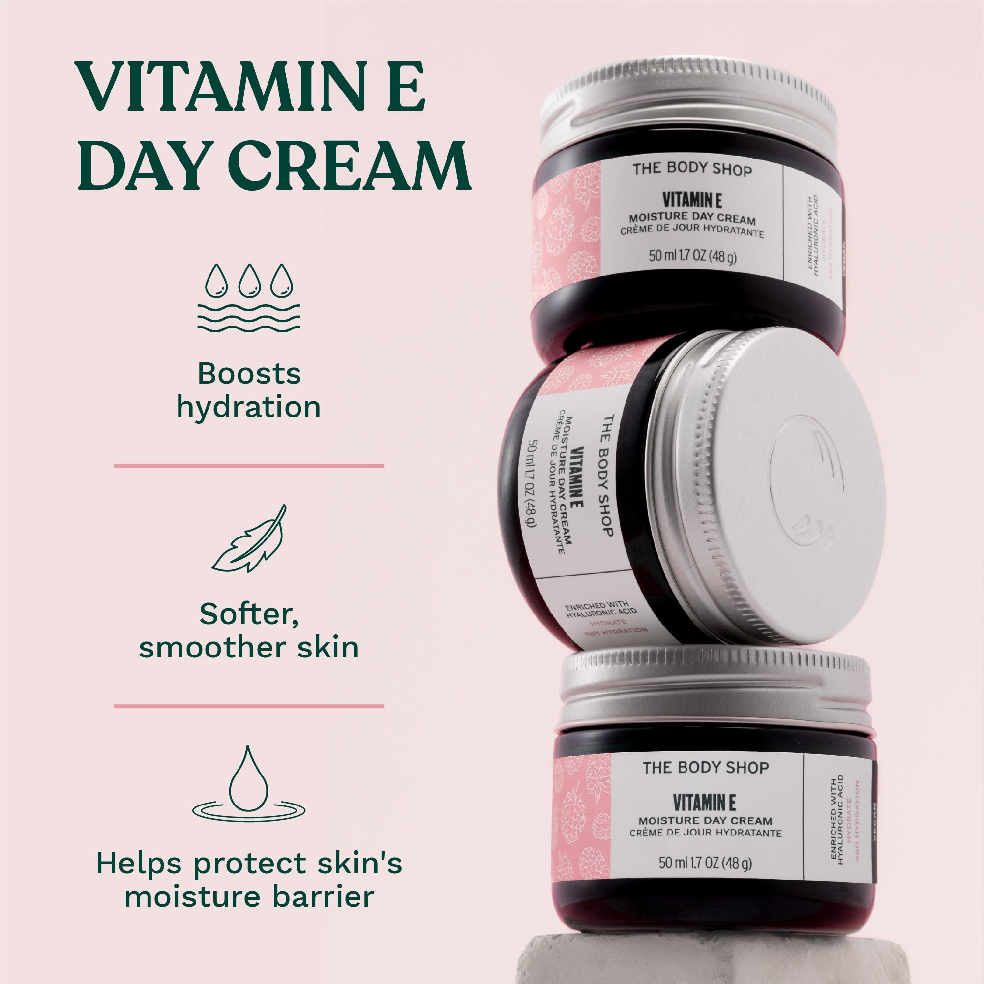 Three jars of The Body Shop Vitamin E Day Cream on a light pink background with text about product benefits. Boosts hydration. Softer, smoother skin. Helps protect skin's moisture barrier.