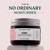 The Body Shop Vitamin E Moisture Day Cream jar on a light pink background with text 'This is No Ordinary Moisturiser'.